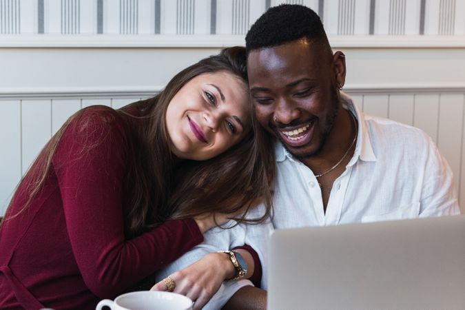 Cheerful multiethnic couple using laptop during breakfast at home