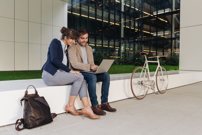 Cheerful colleagues using laptop on street