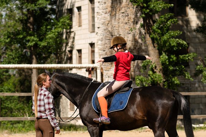 Child rider practices balance on horse guided by instructor.