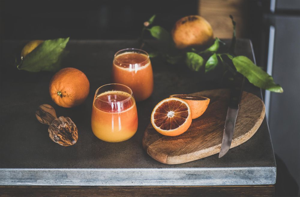 Two glasses of freshly squeezed blood orange juice, with squeezer
