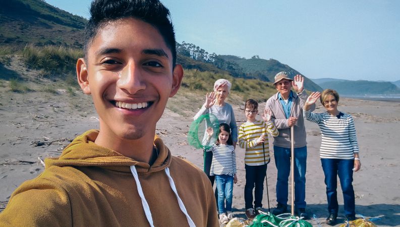 Young man taking selfie to group of volunteers after cleaning beach