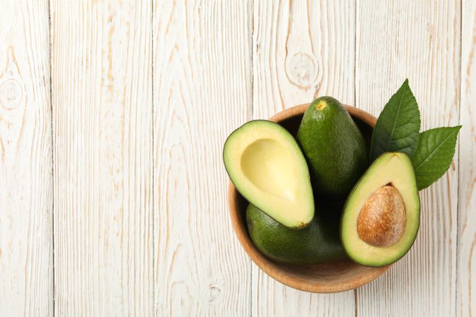 Bowl with fresh avocado on wooden background, top view