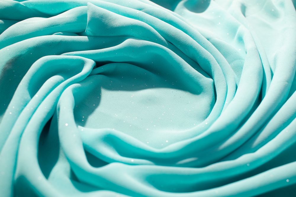 Spiral Twisted Turquoise wavy crumpled fabric with little sparkling dust and copy space in center, texture and  background.