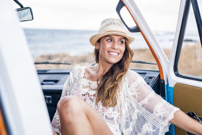 Smiling woman in hat in front seat of car opening door