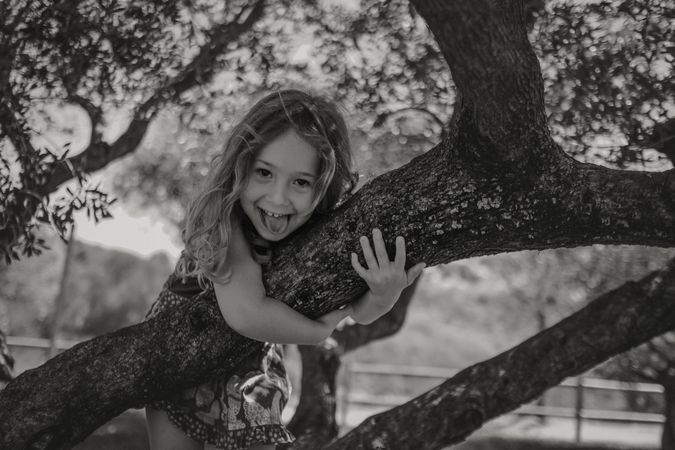 Smiling girl climbing tree in sunny day