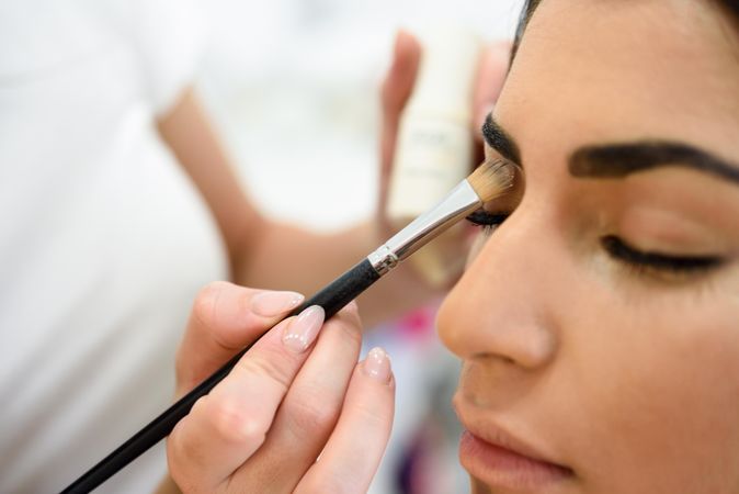 Brush applying eye shadow to woman’s eyes from palette