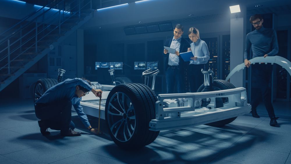 Team of Automotive Engineers Working on Electric Car Platform Chassis, Taking Measures, working with 3D CAD Software