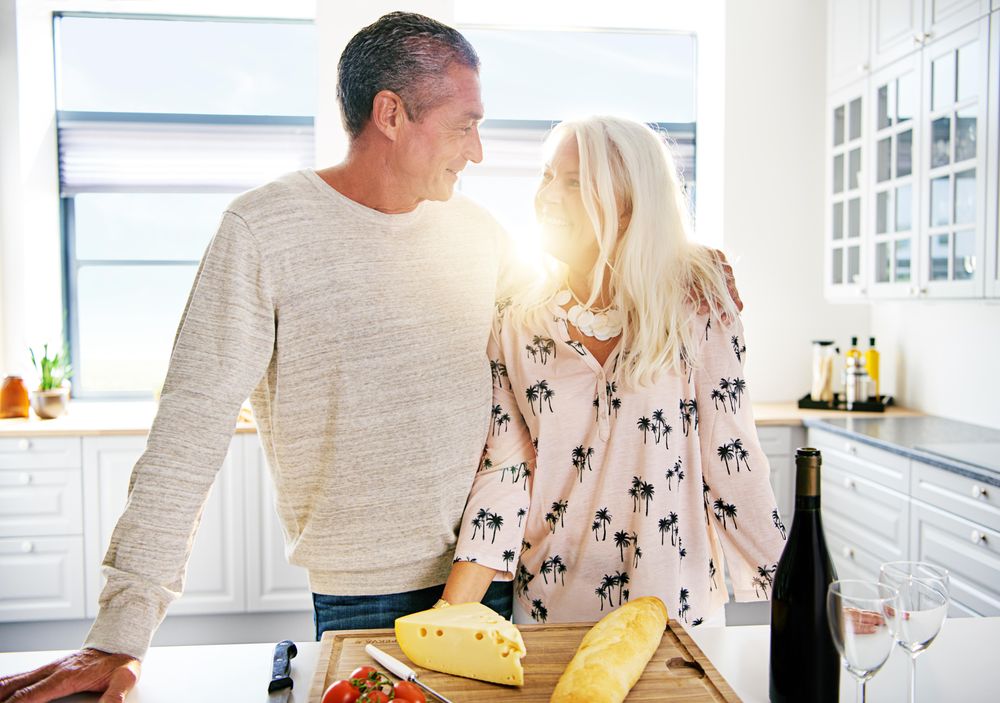Older couple in a bright kitchen with cheese, baguette and wine