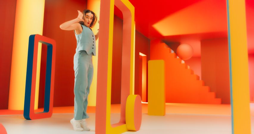 Portrait of Stylish Female Dancer Performing in a Funky Colorful Decorated Studio While Looking at Camera. Woman Dancing in Abstract Environment, Jumping Through Geometric Shapes