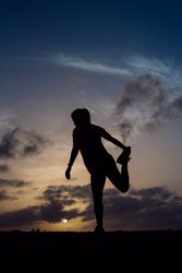 Stretching woman and sky with clouds at sunset