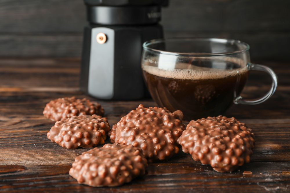 Chocolate cookies and cup of coffee on wooden table against dark background