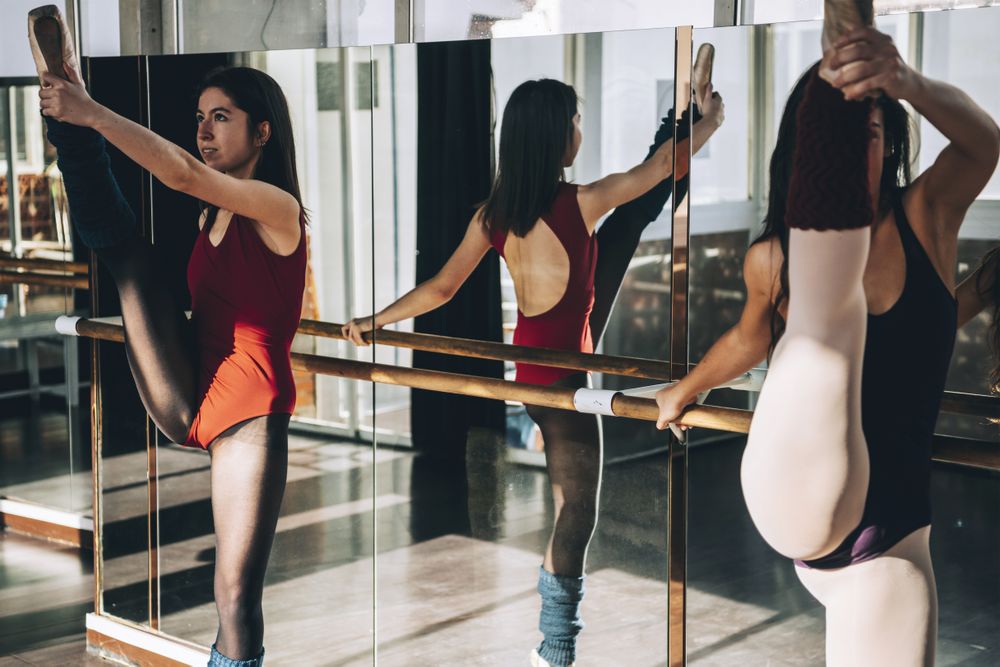 Young flexible ballerinas training in sunny studio and stretching muscles.