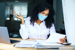 Woman frustrated while reading over documents with a laptop while wearing a facemask 5aZ3d4