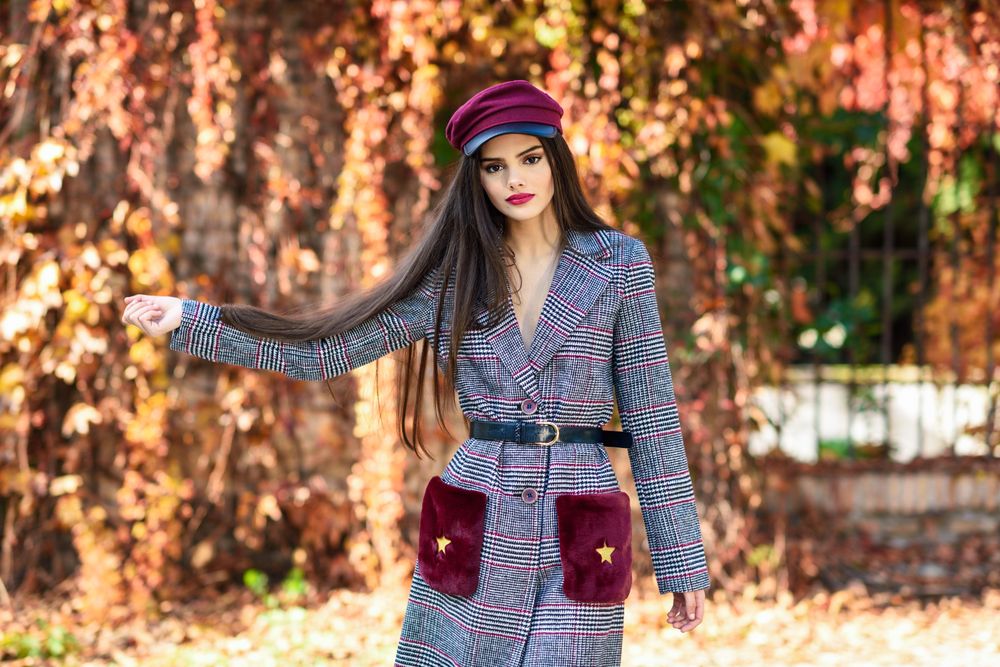 Female in warm winter clothes standing in park with colorful autumn leaves holding her hair
