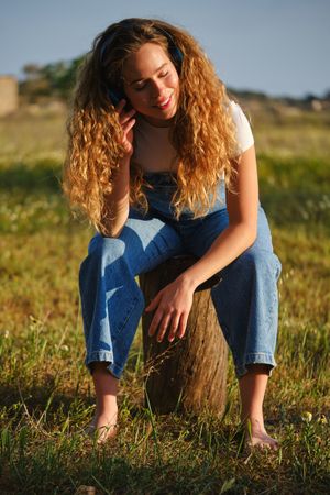 Smiling woman listening to music in headphones on grassy lawn