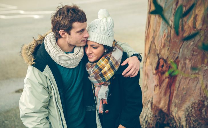 Affectionate couple in winter coats embracing under tree