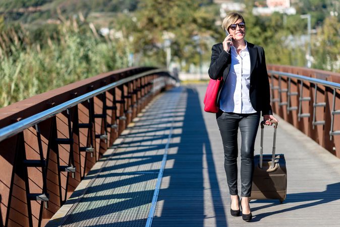 Happy woman walking across bridge with roller suitcase