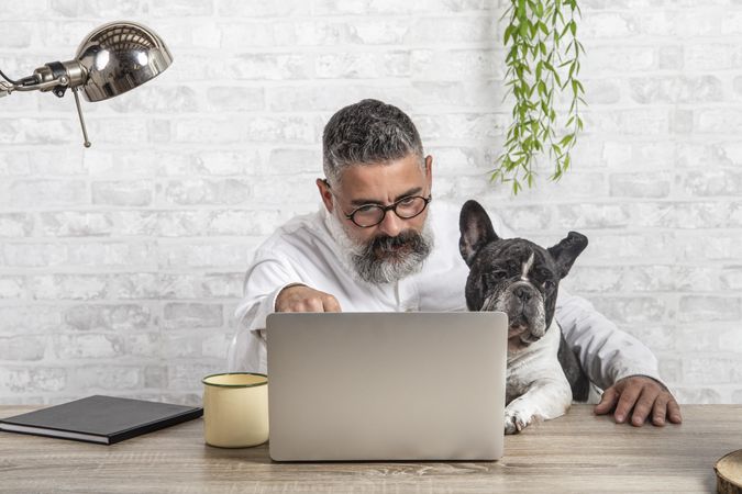 Middle aged man working on his laptop beside his dog at home