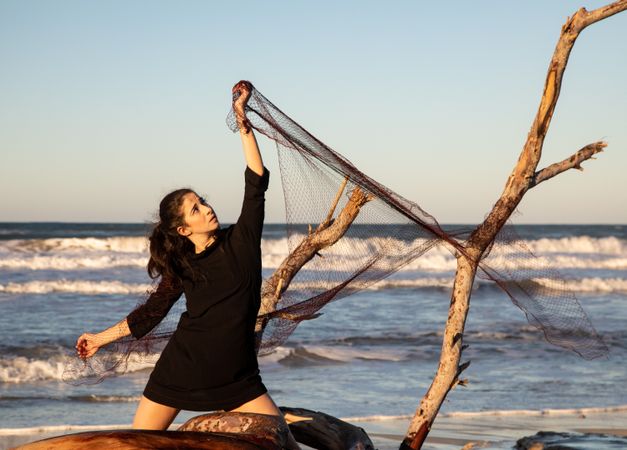Woman in fishing net fixed on twig near water on shore