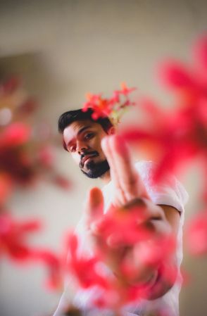 South Asian man in light shirt beside red flowers