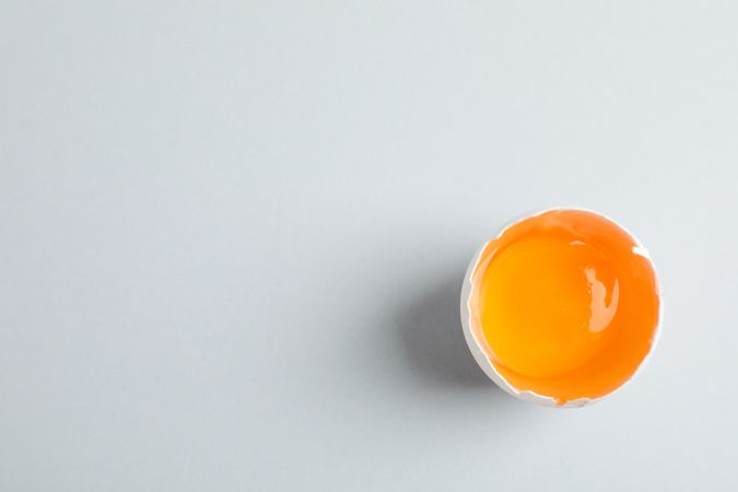 Half broken egg with yolk on grey background, space for text and top view