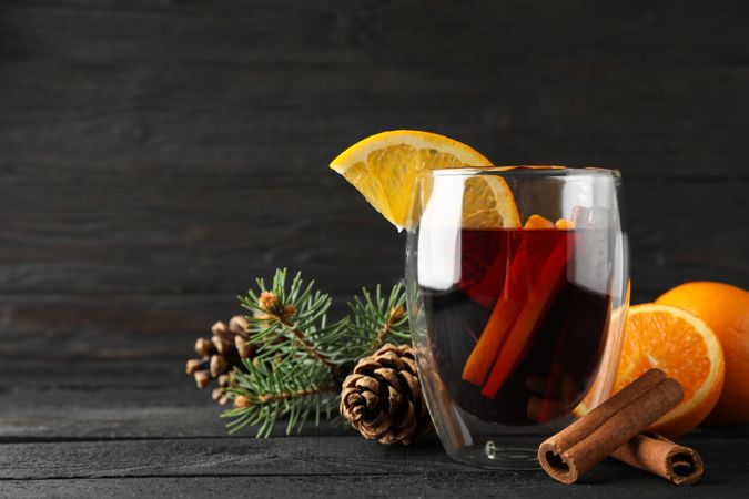 Glass of tasty mulled with orange on decorated background, space for text