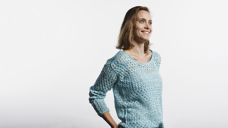 Happy woman wearing a woollen top standing against neutral background