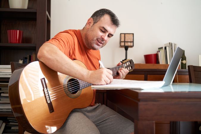 a man with a laptop computer in online guitar lessons writes scales and chords