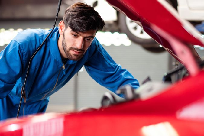 Man looking at open engine of red car auto repair shop