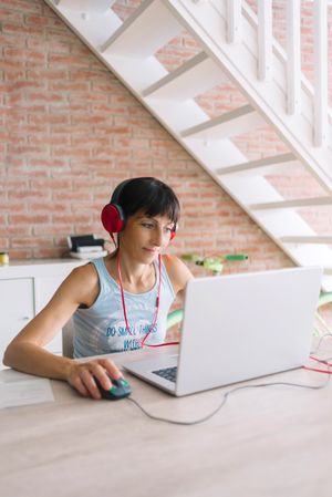 Woman wearing headphones while working at laptop in loft