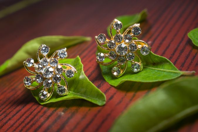 Close-up of beautiful luxury diamond earrings on green leaves with a wood background