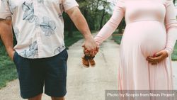Pregnant woman and man holding hands and holding baby shoes outdoor 0vW8R5