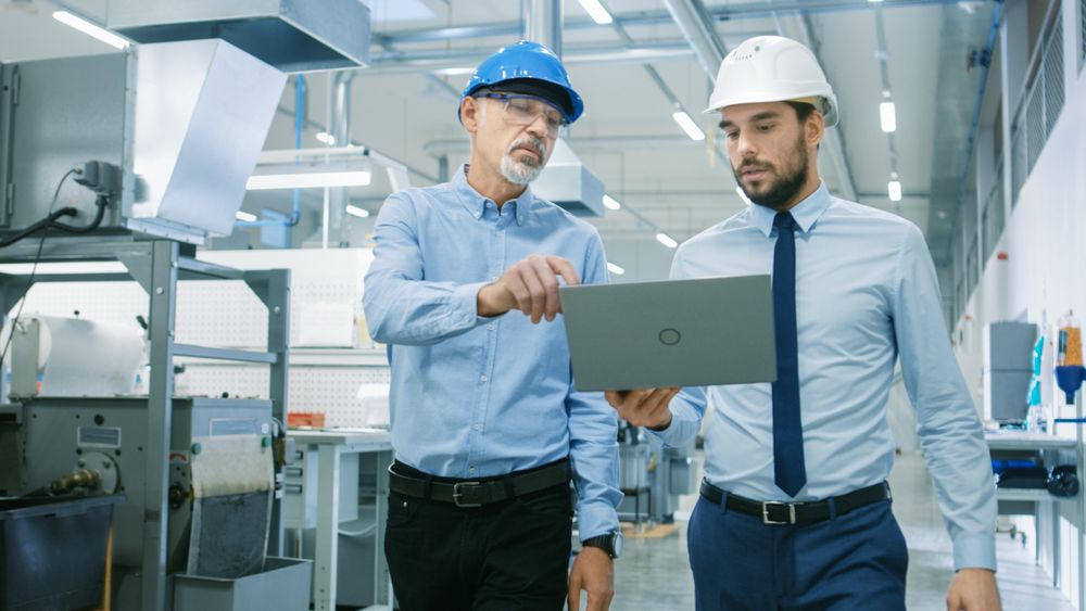 Head of the Department Holds Laptop and  Discuss Product Details with Chief Engineer while They Walk Through Modern Factory.