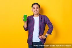 Asian man with hand on hip in plaid shirt holding smartphone with chroma key 0LeOP5