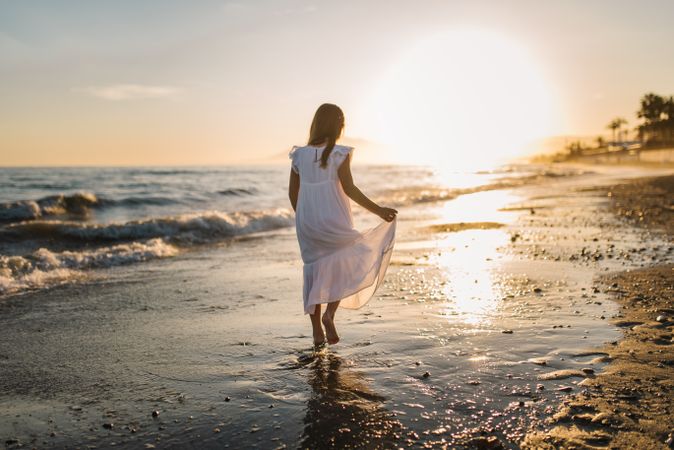 Adorable girl walking on seaside at sunset