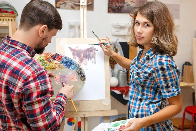 A man and woman draw an abstract painting with oil paints on easel