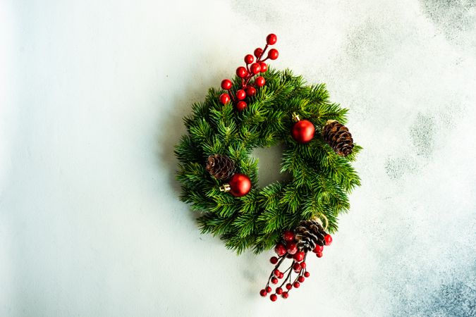 Christmas wreath with red baubles, pine cones and holly on marble counter