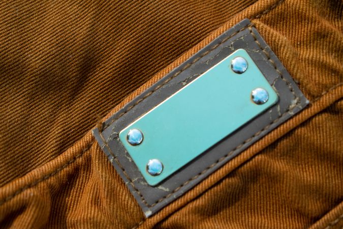 Blank shiny metallic label on bright brown jeans, fabric texture mockup