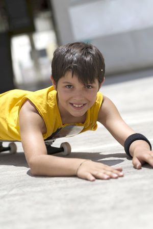 Young smiling boy lying on a skateboard while looking camera on a bright day