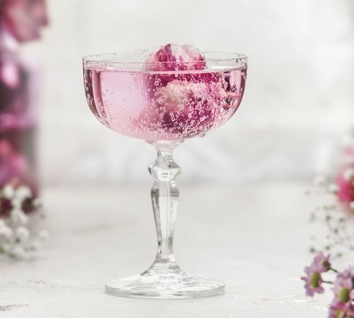 Close up of sparkling pink drink with rose petals in champagne glass