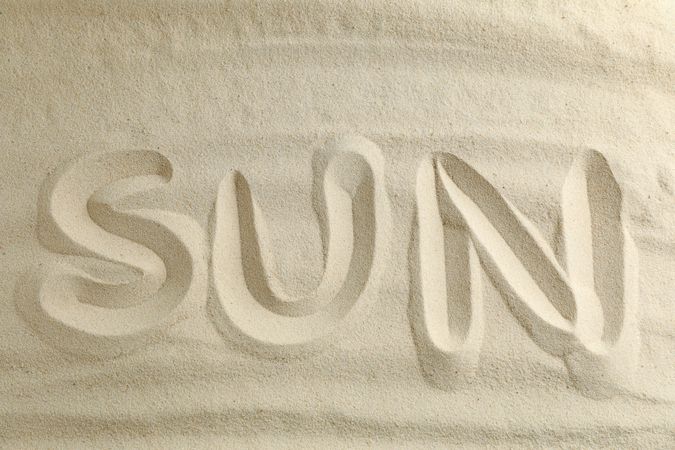Clear sea sand with inscription sun, space for text and top view. Summer vacation background