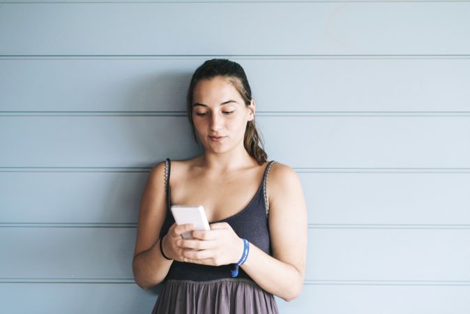 Teenage female using cell phone while leaning against wood paneled wall