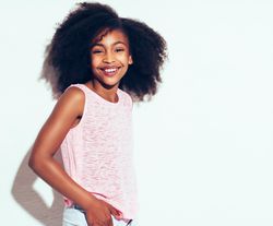 Studio portrait of young girl smiling in pink vest with hands in pocket