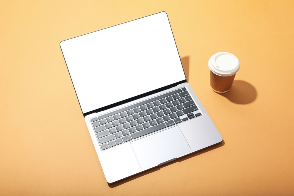 Top view of laptop with mockup screen and to go coffee on light orange desk