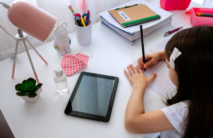 Girl studying at home with tablet and mask on table