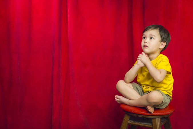 Boy Sitting on Stool in Front of Curtain