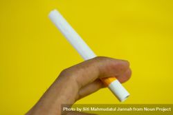 Side view of hand holding cigarette on yellow background bGRN9x