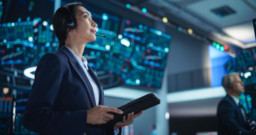 Female Investment Banker Wearing Headphones and Using a Tablet Computer with Financial Market Analytics Data.