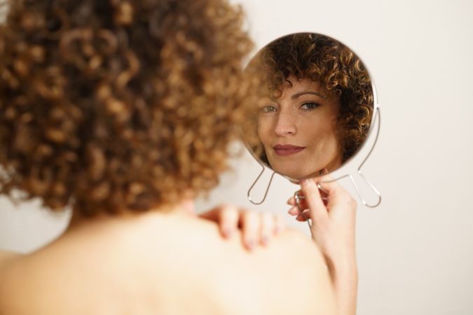 Back of content female and her reflection in hand mirror