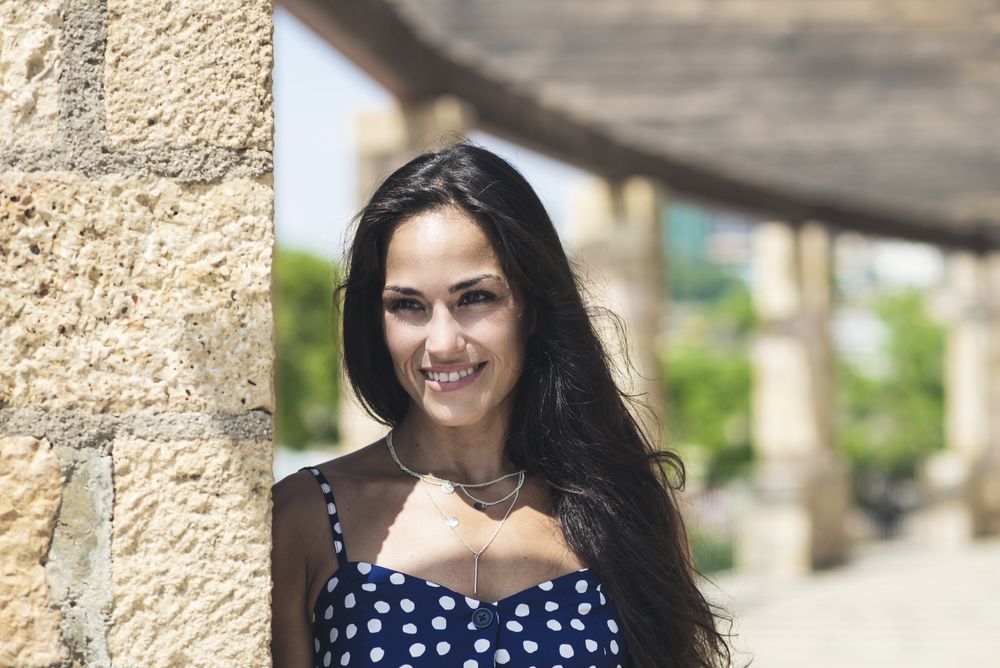 Beautiful hispanic woman in blue dress leaning on wall while wistfully looking away